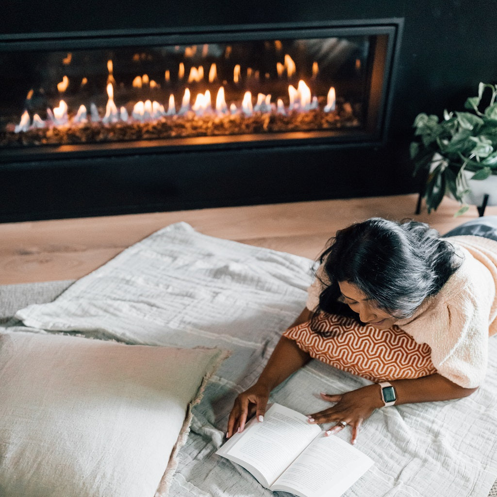 woman reading book laying on floor near modern fireplace