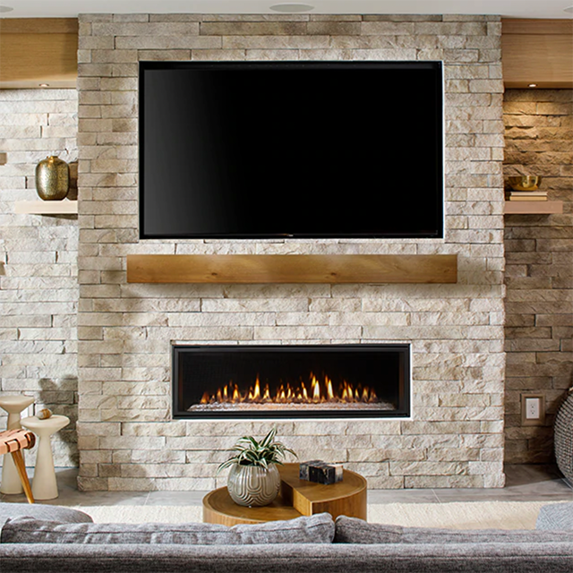 A stone wall of a living room which houses a large TV and fireplace.