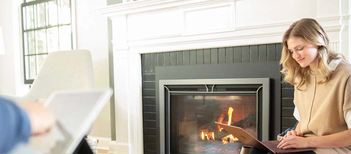 A woman uses her laptop while warming up in front of a fireplace