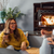 woman in glasses and yellow sweater sitting on floor drinking red wine with friends in front of harman pellet stove insert