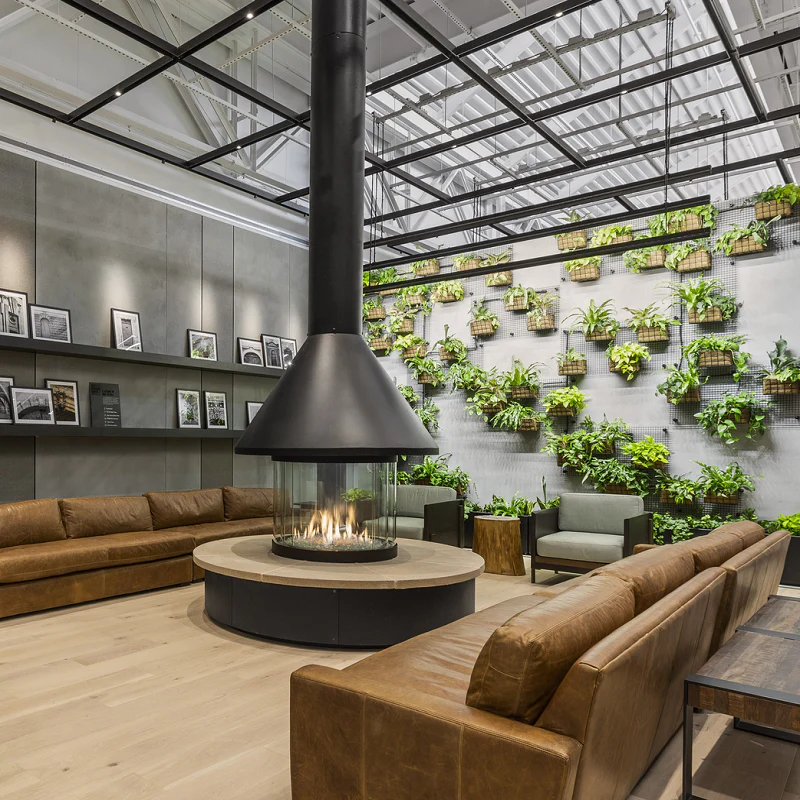 custom round gas fireplace in lobby with plants on wall and brown leather couches